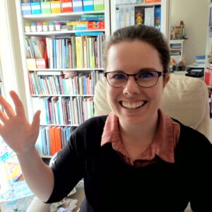 Bronwyn is sitting in her office. She is smiling and waving at the camera.